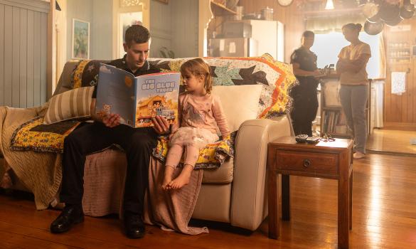 Officer reading to child; another officer speaks to adult in background