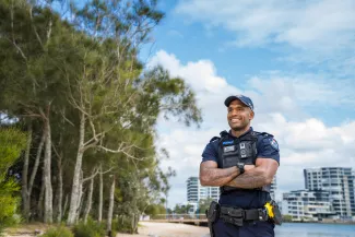 Smiling Queensland police officer standing on beach with arms folded